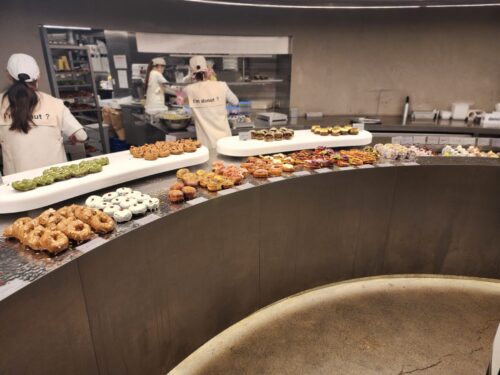 「I'm donut ?」のロゴ入りユニフォームを着たスタッフたちが、カウンター内でドーナツの提供や調理を行っている様子。