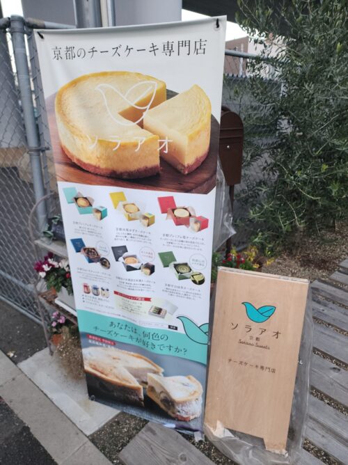 店舗前に掲示されているメニュー看板。プレーン、抹茶、チョコなど色とりどりのチーズケーキの写真と解説が掲載されている。